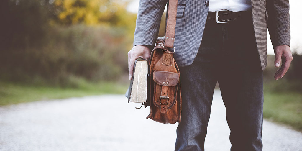 Das Bild zeigt einen Mann mit einer Tasche und Buch in der Hand